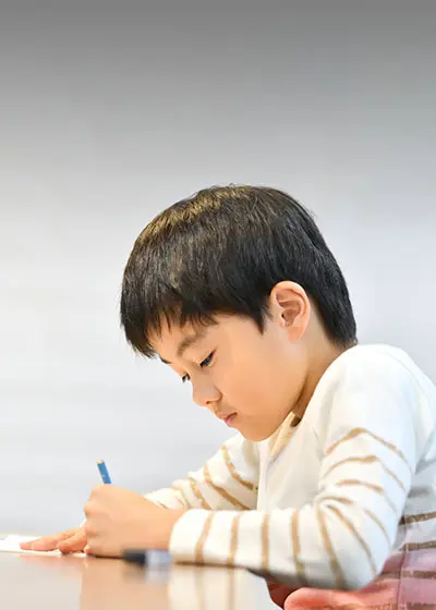 写真：小学校低学年の男の子が机に向かって勉強をしている